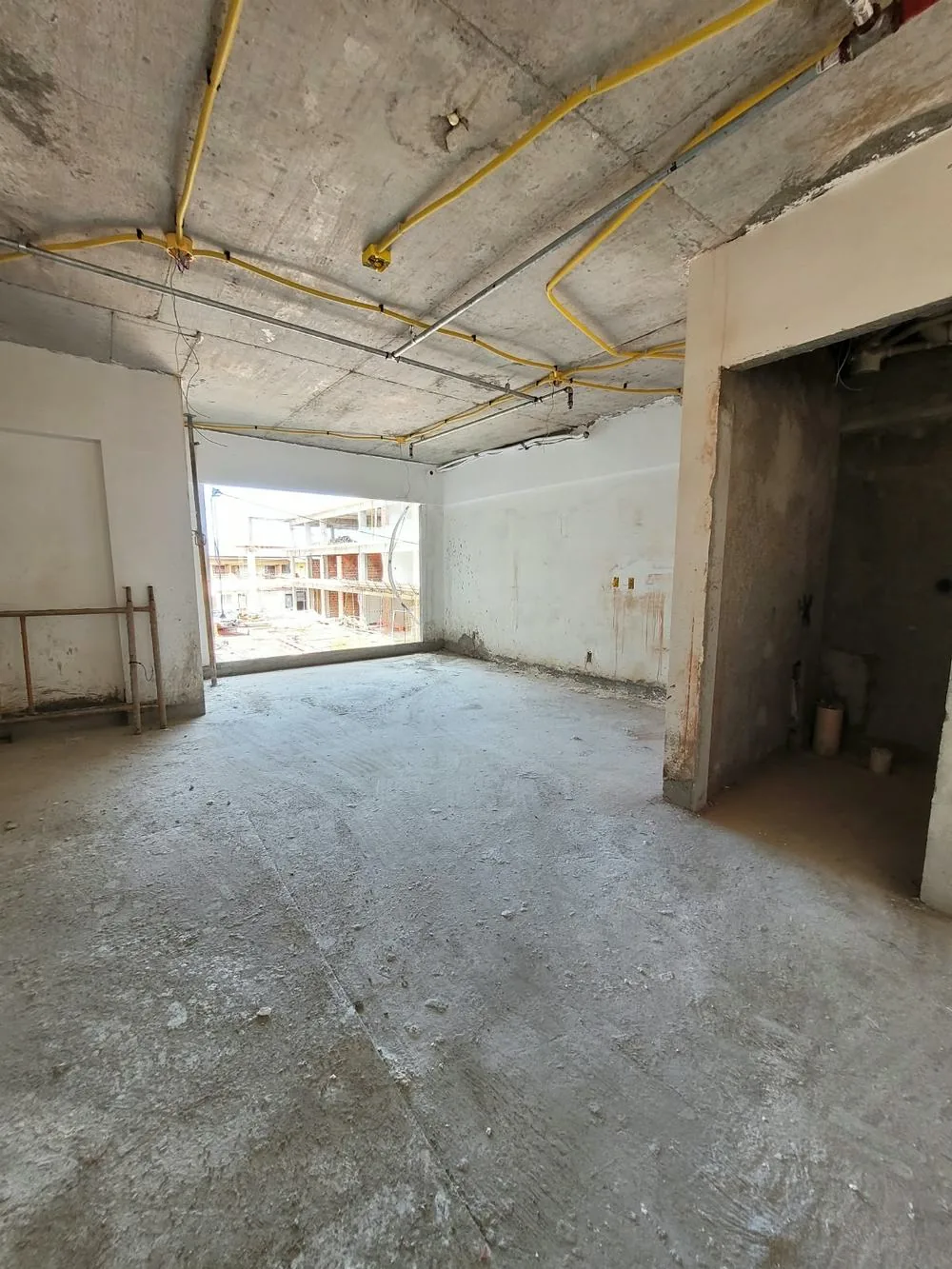 Interior de uma unidade em construção, com instalações no teto e janela ampla